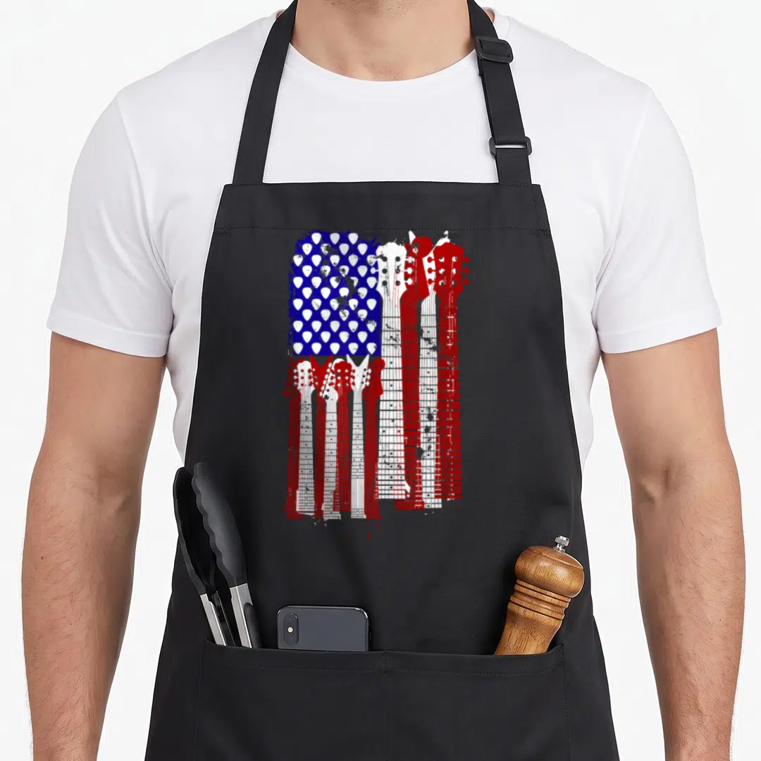Plectrum american flag apron - Guitar necks and plectrums forming a distressed American flag in red white and blue — shown on a black cotton canvas apron against a white background