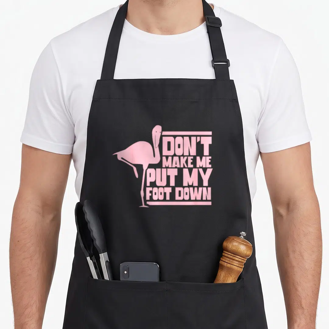 Foot animal flamingo apron - Pink flamingo silhouette standing on one leg beside stacked text 'DON'T MAKE ME PUT MY — shown on a black cotton canvas apron against a white background