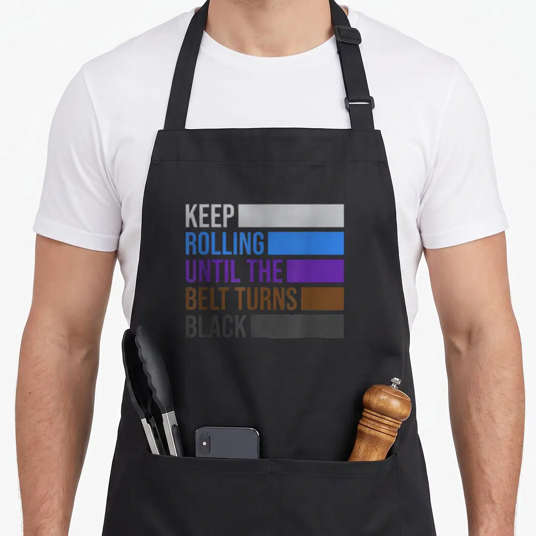 Rolling jitsu quotes apron - Stacked text next to five colored bars representing martial arts belt progression levels — shown on a black cotton canvas apron against a white background