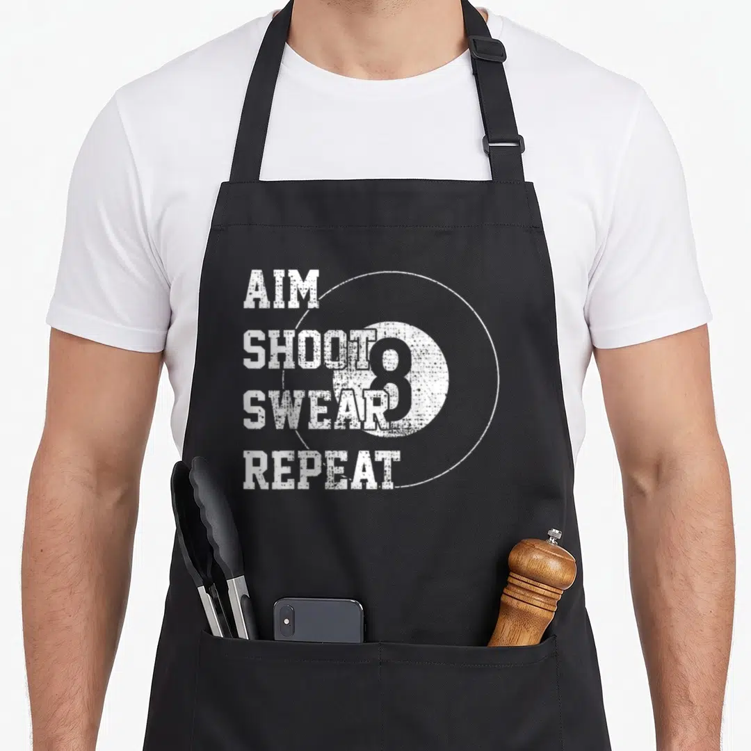 Ball billiards lover apron - White distressed AIM SHOOT SWEAR REPEAT text next to a large 8-ball inside a thin circle — shown on a black cotton canvas apron against a white background