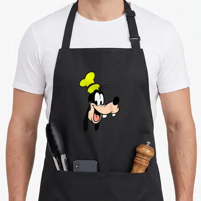 Single lemon apron - Cartoon dog head with yellow chef hat, black body, tan face, facing right — shown on a black cotton canvas apron against a white background