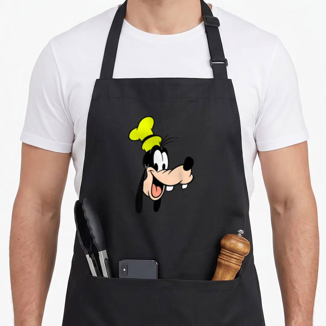 Single lemon apron - Cartoon dog head with yellow chef hat, black body, tan face, facing right — shown on a black cotton canvas apron against a white background