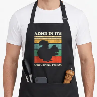 Original squirrel aprons - ADHD IN ITS ORIGINAL FORM text over squirrel silhouette and retro colored stripes — shown on a black cotton canvas apron against a white background