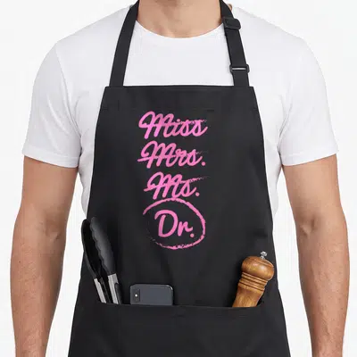 Doctorate mrs apron - Pink stacked text Miss Mrs Ms Dr with hand-drawn circle around Dr — shown on a black cotton canvas apron against a white background