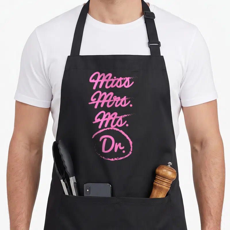 Doctorate mrs apron - Pink stacked text Miss Mrs Ms Dr with hand-drawn circle around Dr — shown on a black cotton canvas apron against a white background