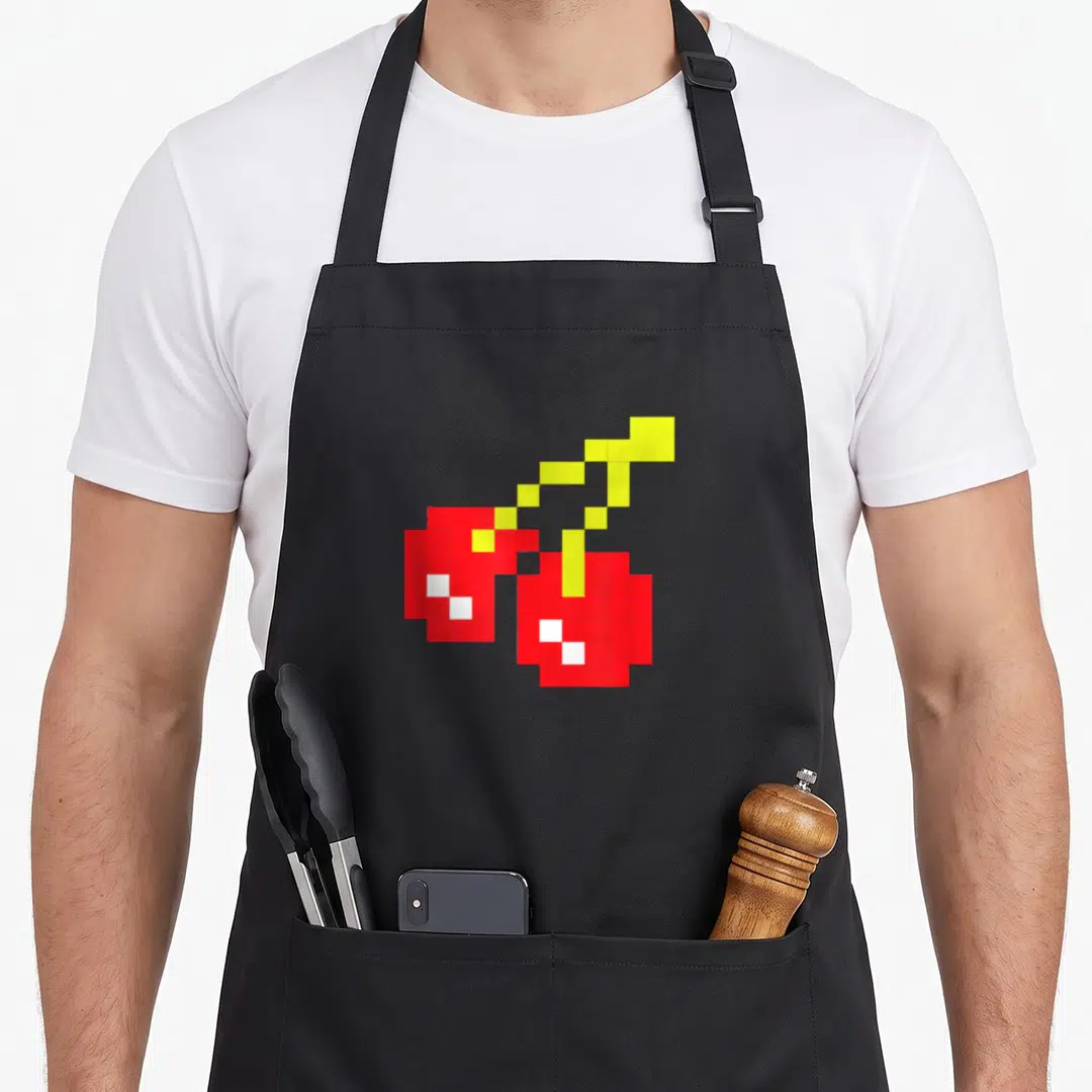 Pixel cherry apron - Two red pixelated cherries with yellow stems and white highlights — shown on a black cotton canvas apron against a white background