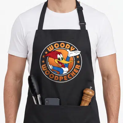 Circle woodpecker apron - Woody Woodpecker cartoon character inside orange circle with stars and orange text — shown on a black cotton canvas apron against a white background