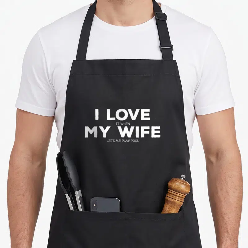 Billiard wife apron - White stacked text reading I LOVE IT WHEN MY WIFE LETS ME PLAY POOL on black background — shown on a black cotton canvas apron against a white background