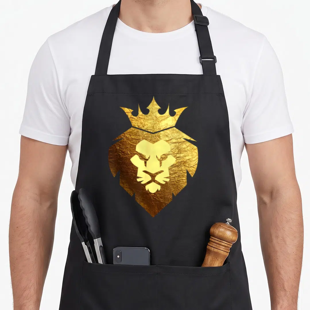 Leo crown royal apron - Gold minimalist lion head with crown on textured background — shown on a black cotton canvas apron against a white background