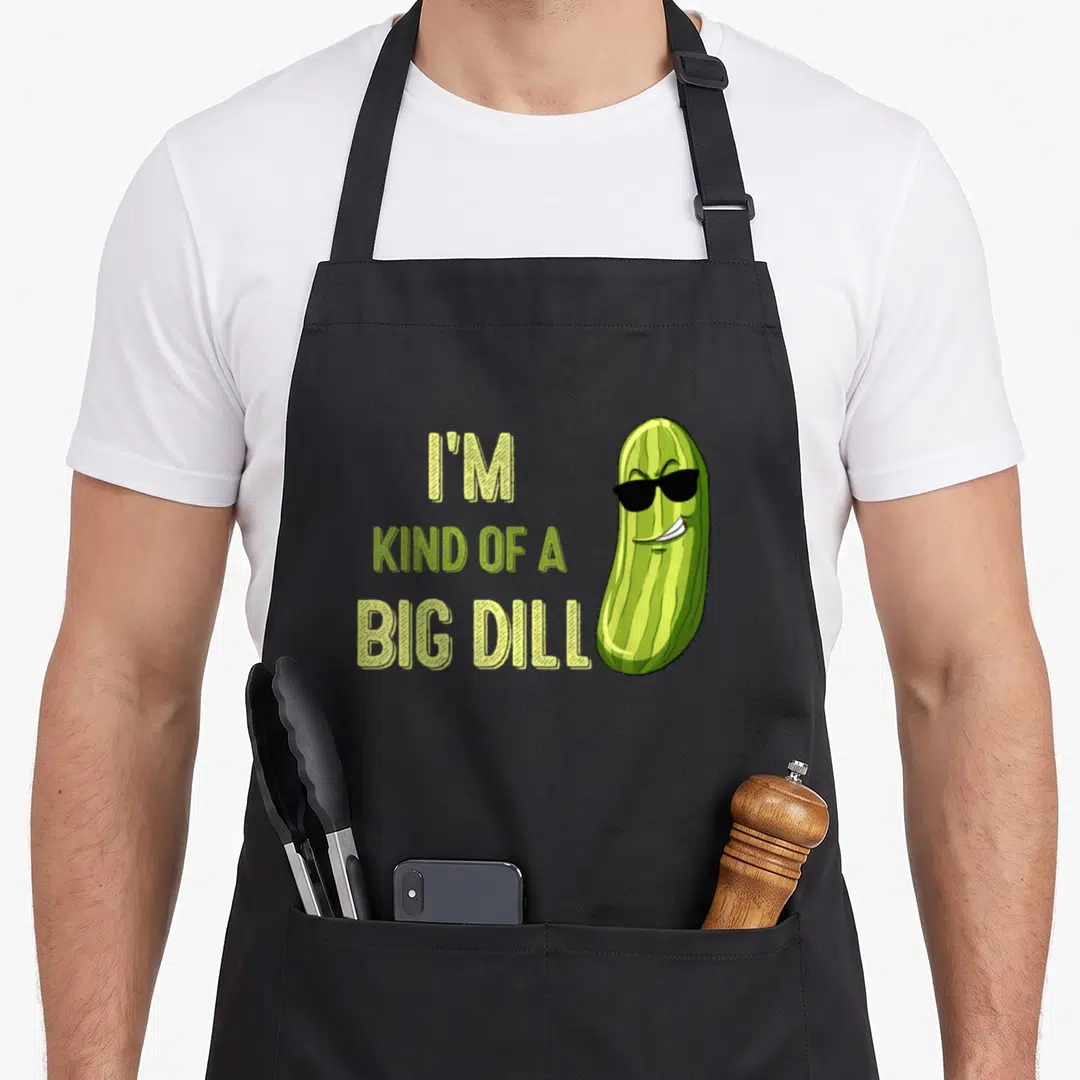 Deal pickle apron - I'M KIND OF A BIG DILL text beside cartoon pickle wearing sunglasses in lime and dark green — shown on a black cotton canvas apron against a white background