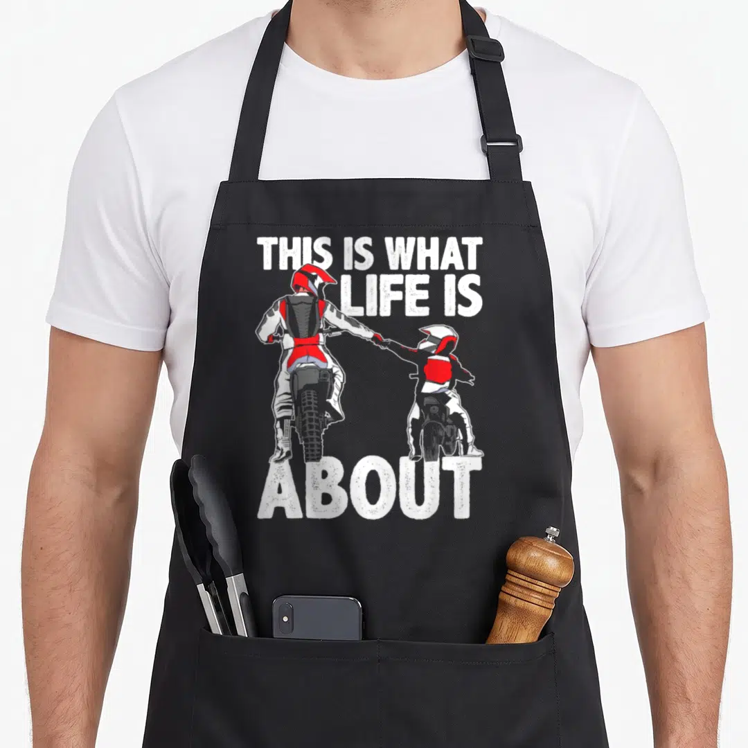 Father bike apron - Two motocross riders holding hands with distressed white textTHIS IS WHAT LIFE IS ABOUT — shown on a black cotton canvas apron against a white background