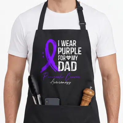 Pancreatic sisters apron - Purple ribbon and I WEAR PURPLE FOR MY DAD text with Pancreatic Cancer Awareness script — shown on a black cotton canvas apron against a white background