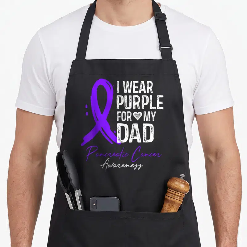 Pancreatic sisters apron - Purple ribbon and I WEAR PURPLE FOR MY DAD text with Pancreatic Cancer Awareness script — shown on a black cotton canvas apron against a white background