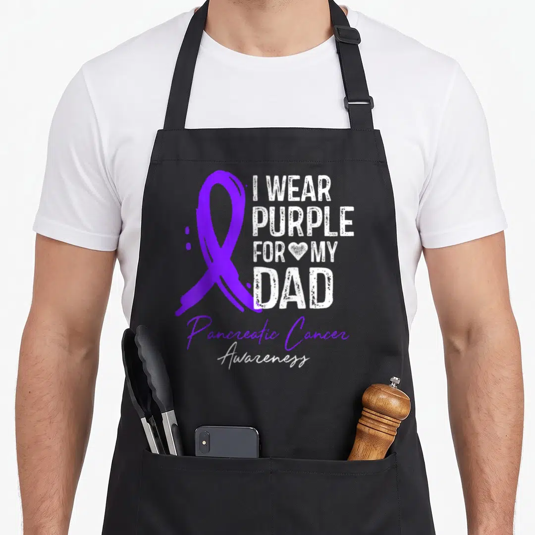 Pancreatic sisters apron - Purple ribbon and I WEAR PURPLE FOR MY DAD text with Pancreatic Cancer Awareness script — shown on a black cotton canvas apron against a white background