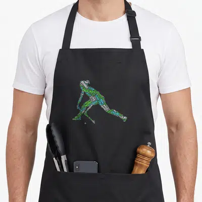 Funny hockey field player apron - Word cloud silhouette of a field hockey player formed by green and orange text terms — shown on a black cotton canvas apron against a white background