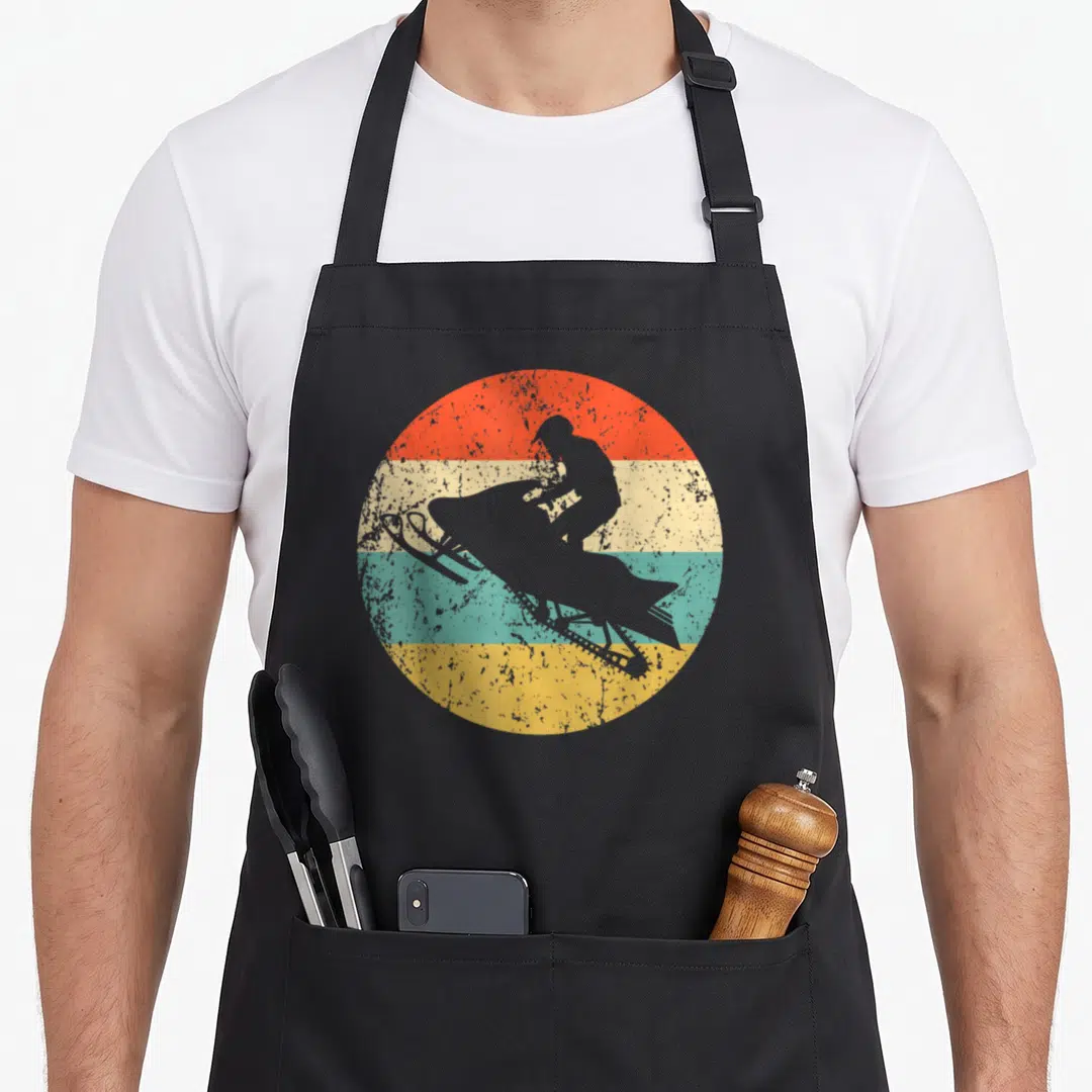 Funny snowmobiling snowmobile girl apron - Grey snowmobile rider silhouette over red beige teal and yellow stripes — shown on a black cotton canvas apron against a white background