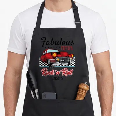 Funny 50s rockabilly apron - Red car over checkered strip with Fabulous Fifties Rock n Roll text — shown on a black cotton canvas apron against a white background