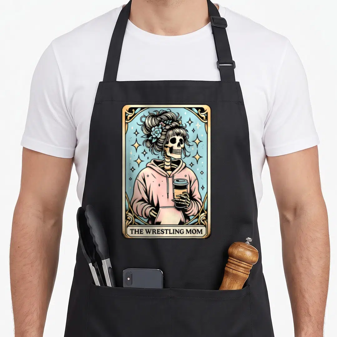 Wrestling skeleton apron - Skeleton in pink hoodie holding coffee inside gold frame with text The Wrestling Mom — shown on a black cotton canvas apron against a white background