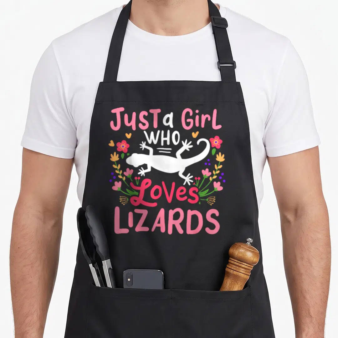 Funny lizard apron - White lizard silhouette with pink text and floral wreath in pink green orange — shown on a black cotton canvas apron against a white background