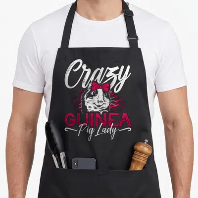 Zoo crazy guinea lady apron - Cartoon guinea pig wearing a pink bow under Crazy GUINEA Pig Lady text — shown on a black cotton canvas apron against a white background