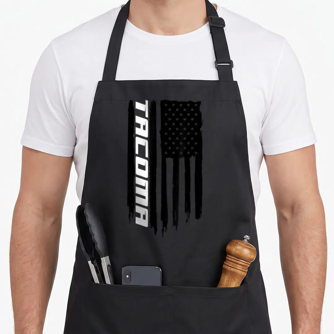 Washington american flag apron - Vertical Tacoma text beside a distressed black and white USA flag with tattered stripes — shown on a black cotton canvas apron against a white background