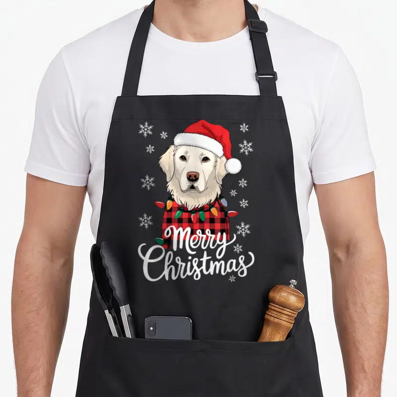 Christmas english aprons - Cartoon cream dog in red plaid scarf with lights and Merry Christmas text — shown on a black cotton canvas apron against a white background