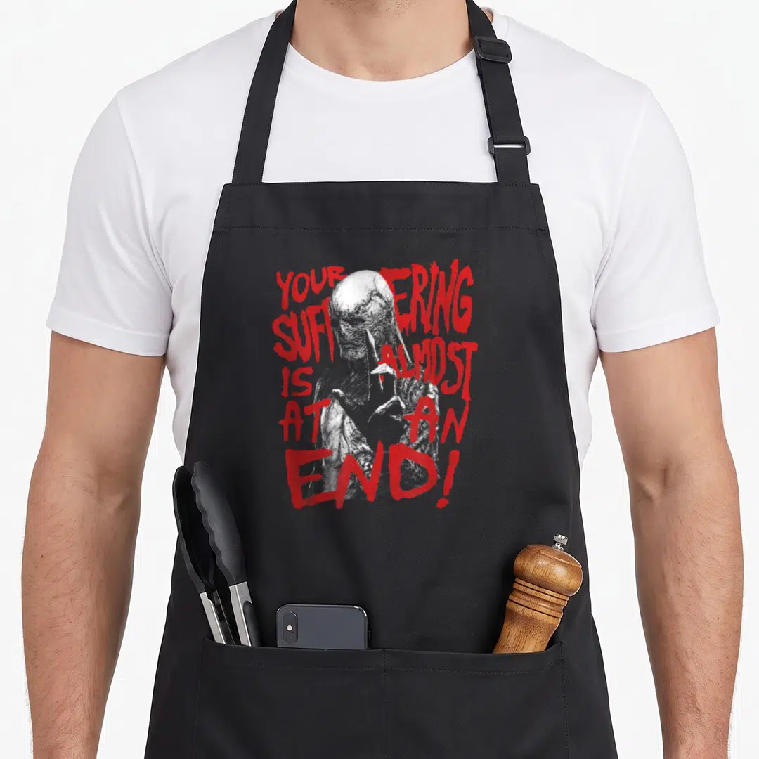 Vecna at apron - Grey zombie figure with red distressed text YOUR SUFFERING IS ALMOST AT AN END — shown on a black cotton canvas apron against a white background