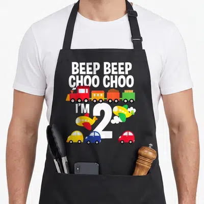 Birthday airplane apron - Beep Beep Choo Choo text with train, cars, planes and large number two — shown on a black cotton canvas apron against a white background