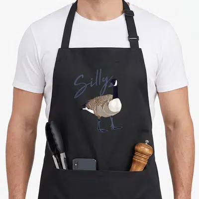 Canadian silly apron - Cartoon goose standing with Silly script in blue-grey behind it — shown on a black cotton canvas apron against a white background