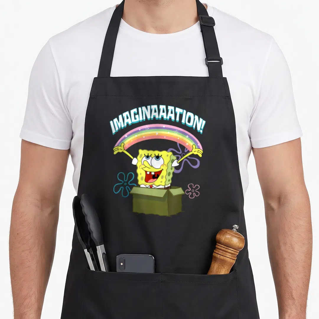 Squarepant box apron - SpongeBob in green box under rainbow with IMAGINAAAATION! text — shown on a black cotton canvas apron against a white background