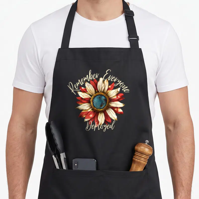 Remember patriotic apron - Red white blue sunflower with Remember Everyone Deployed script text — shown on a black cotton canvas apron against a white background