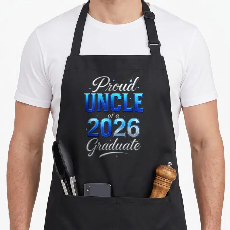 Uncle diploma apron - Stacked blue and white Proud UNCLE of a 2026 Graduate text with small stars — shown on a black cotton canvas apron against a white background
