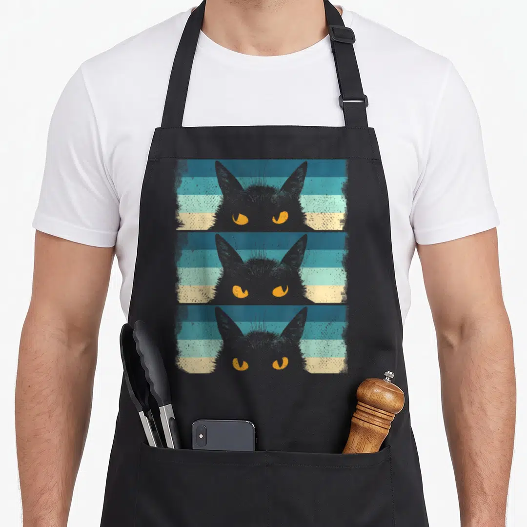 Cute kitten grumpy cat apron - Three grey cat heads with yellow eyes stacked vertically over blue teal and cream stripes — shown on a black cotton canvas apron against a white background