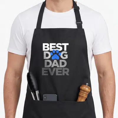 Husband dog dad apron - Stacked white text BEST DOG DAD EVER with blue paw print over the O in DOG — shown on a black cotton canvas apron against a white background