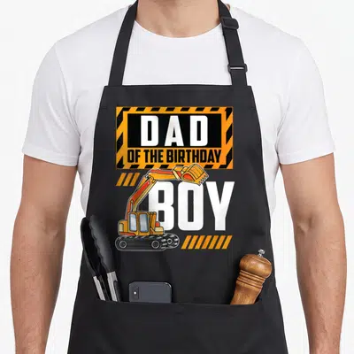 Excavator birthday vehicle apron - Dad of the Birthday Boy text with orange cartoon excavator and striped construction — shown on a black cotton canvas apron against a white background