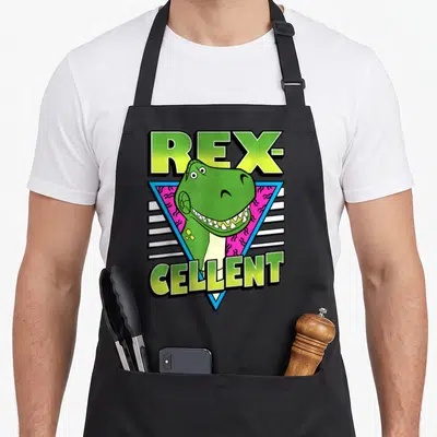 Rex dog breed aprons - REX-CELLENT pun with green T-Rex head in blue triangle on pink zigzag background — shown on a black cotton canvas apron against a white background