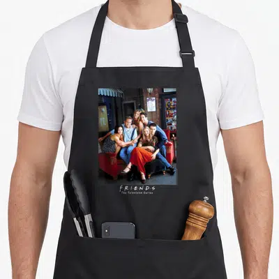 Outside friends apron - Photo of six people on red armchairs with F·R·I·E·N·D·S The Television Series text below — shown on a black cotton canvas apron against a white background