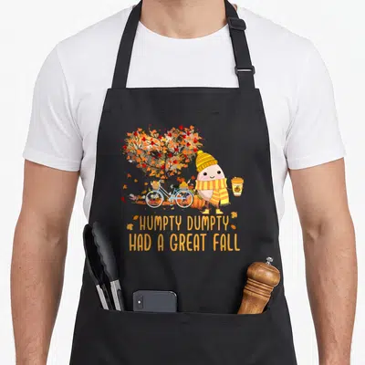 Season cute fall aprons - Humpty Dumpty cartoon with bike pumpkin and great fall text — shown on a black cotton canvas apron against a white background
