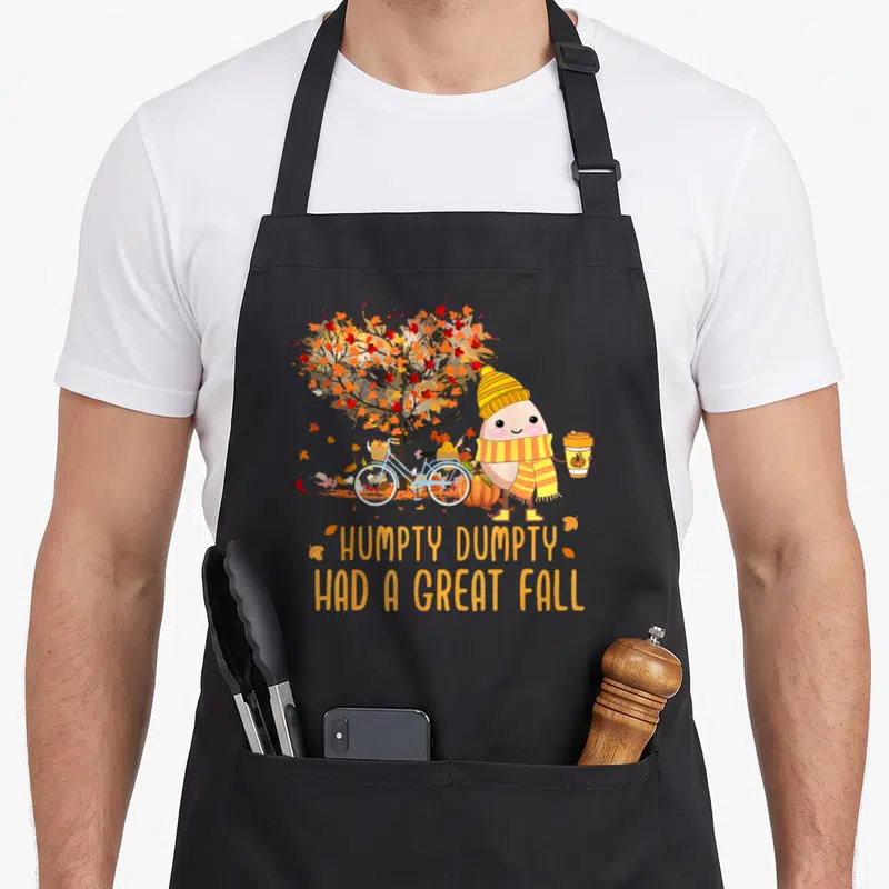 Season cute fall aprons - Humpty Dumpty cartoon with bike pumpkin and great fall text — shown on a black cotton canvas apron against a white background