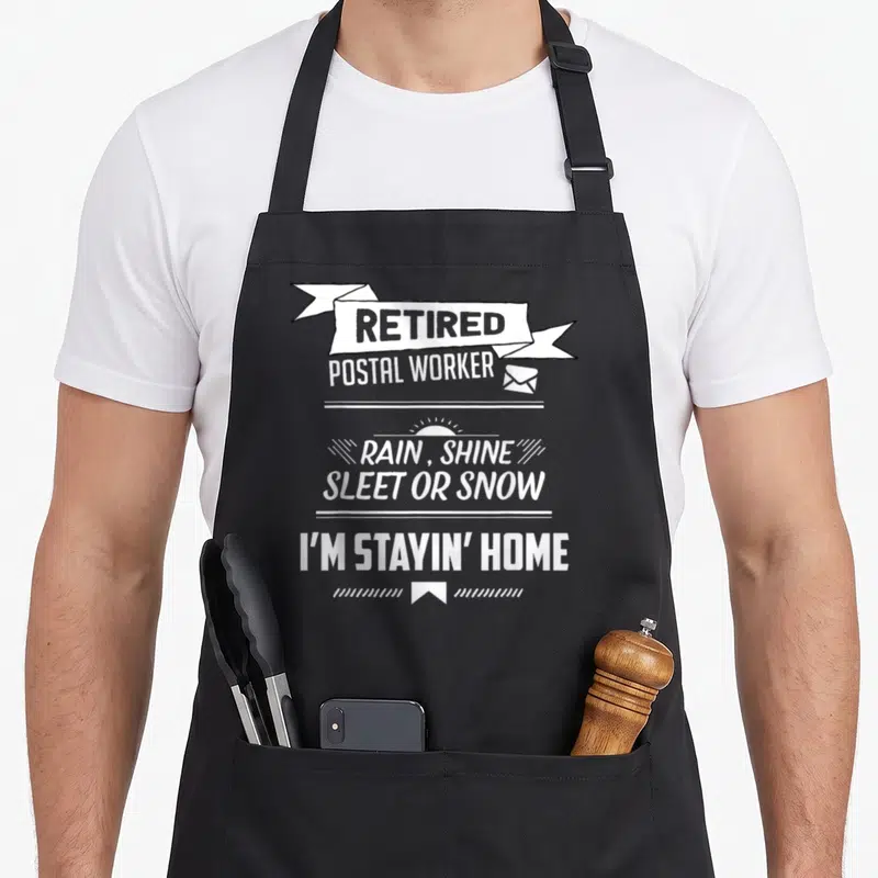 Rain postal aprons - White stacked text reading retired postal worker rain shine sleet or snow I'm stayin' home — shown on a black cotton canvas apron against a white background