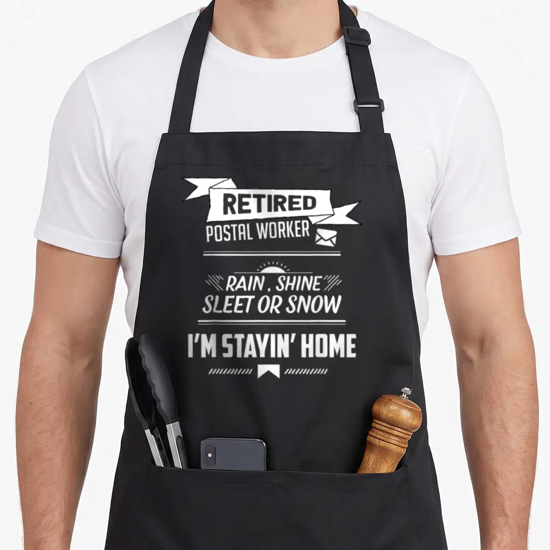 Rain postal aprons - White stacked text reading retired postal worker rain shine sleet or snow I'm stayin' home — shown on a black cotton canvas apron against a white background
