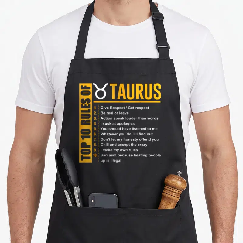 Birthday taurus aprons - Yellow and white Top 10 Rules of Taurus typography with zodiac symbol — shown on a black cotton canvas apron against a white background