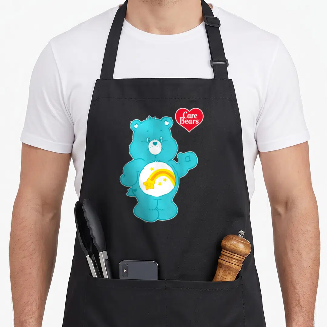 Wish care apron - Blue cartoon bear with rainbow and stars on belly next to red heart logo — shown on a black cotton canvas apron against a white background