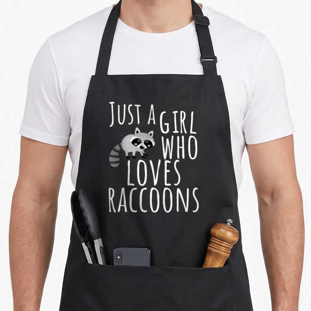 Trash garbage lover apron - Just A Girl Who Loves Raccoons text with grey cartoon raccoon — shown on a black cotton canvas apron against a white background