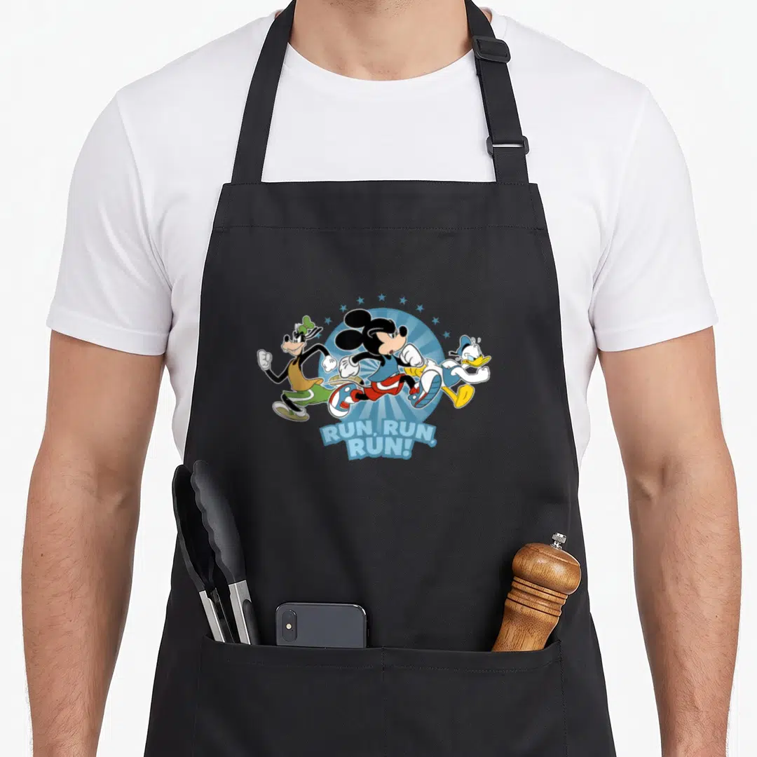 Donald marathon apron - Three cartoon characters running forward under blue sunburst with curved text below — shown on a black cotton canvas apron against a white background