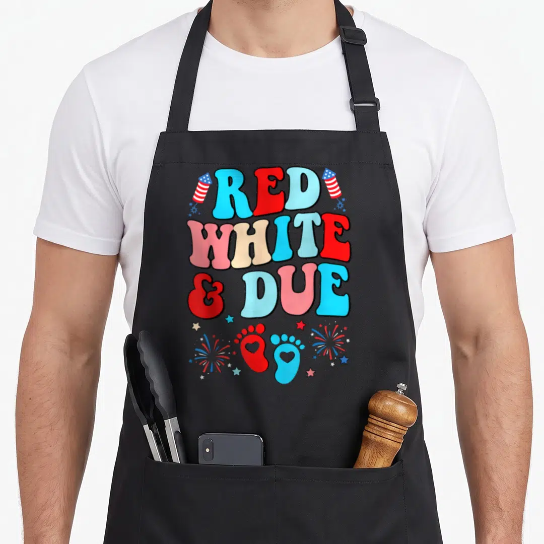 Due pregnancy 4th of july apron - Bubbly text reading RED WHITE & DUE flanked by flags with baby footprints — shown on a black cotton canvas apron against a white background