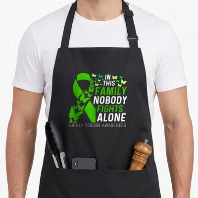 Fighting family aprons - Green ribbon with white text and flying butterflies for kidney disease awareness — shown on a black cotton canvas apron against a white background