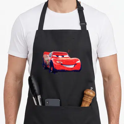 Mcqueen paint apron - Red race car surrounded by red and blue paint splatters on canvas — shown on a black cotton canvas apron against a white background