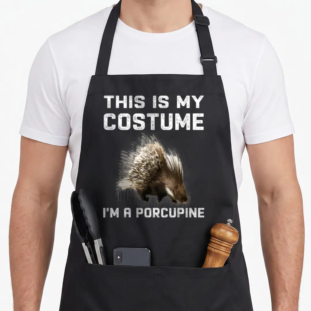 Porcupine halloween apron - Realistic porcupine illustration between white text reading THIS IS MY COSTUME and I M — shown on a black cotton canvas apron against a white background