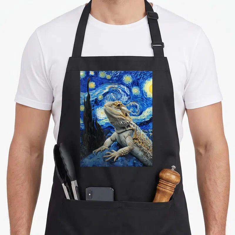 Bearded van gogh apron - Realistic bearded dragon against swirling blue starry night sky with cypress tree — shown on a black cotton canvas apron against a white background